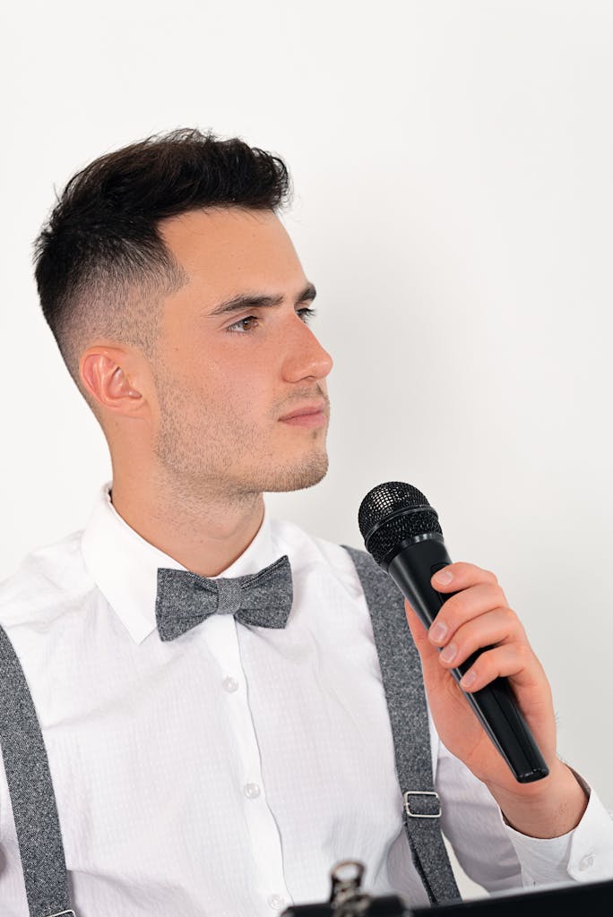 Young caucasian man in white shirt and bow tie holding a microphone looking serious